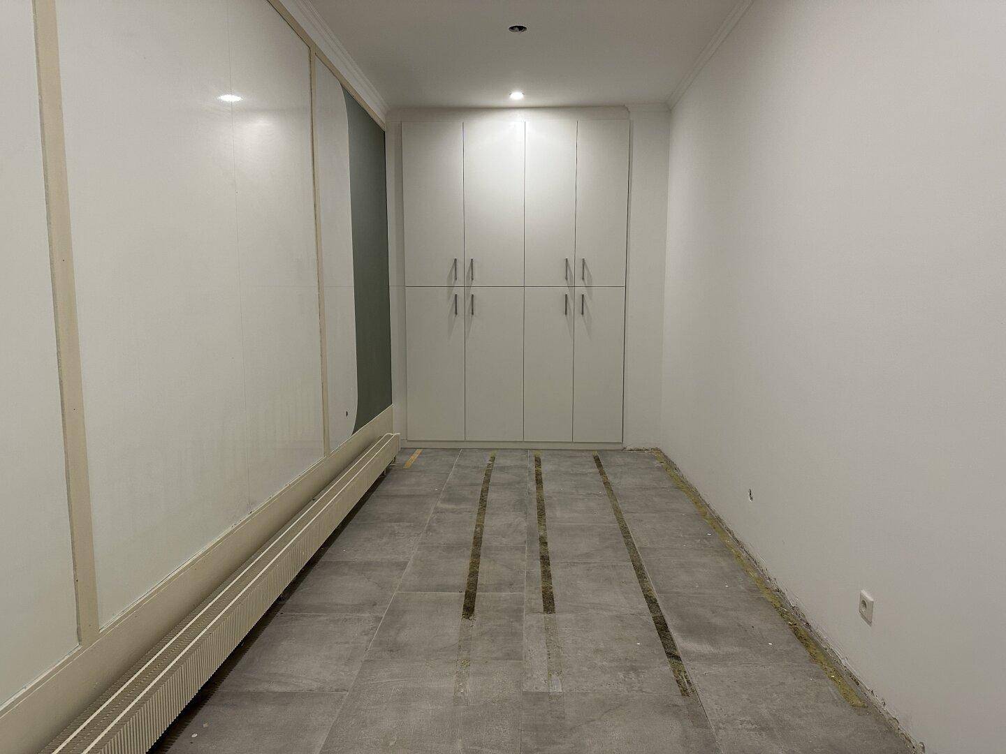 Langer Raum mit Einbauschränken, Fliesenboden und Heizkörpern entlang der Wand.
