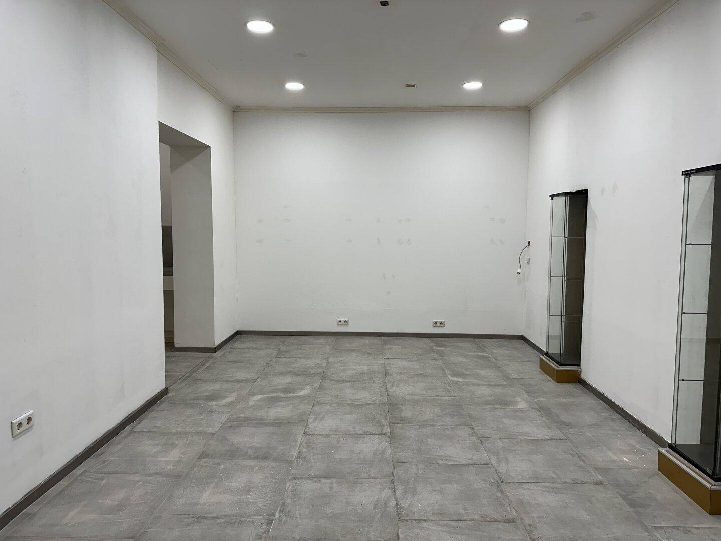 Großer, leerer Geschäftsraum mit Fliesenboden und Einbauschränken an der Wand.