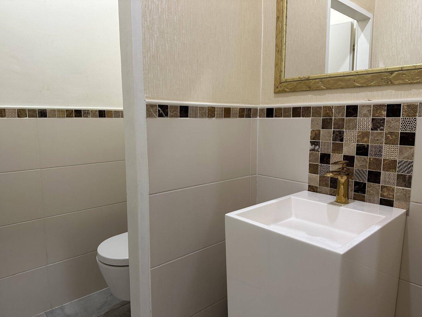 Kleines Gäste-WC mit modernem Waschbecken, Wand-WC und dekorativen Fliesen.