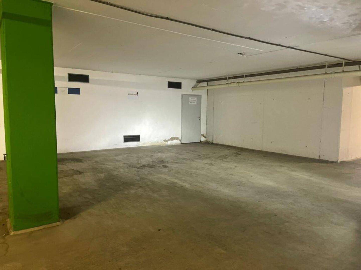 Geräumige Tiefgarage oder Lagerfläche mit Betonboden und grünem Stützpfeiler.