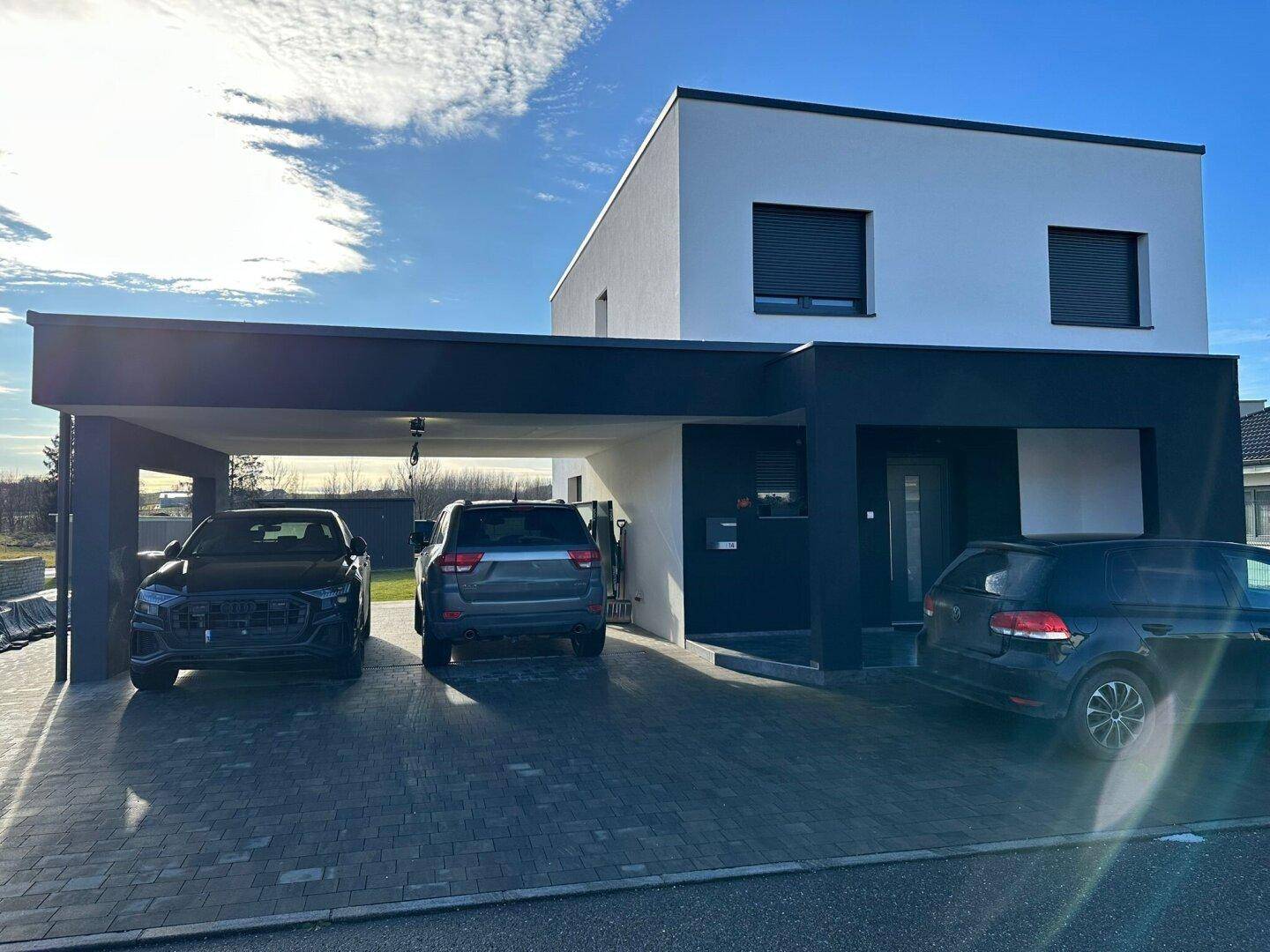 Modernes Einfamilienhaus mit weißer Fassade, schwarzem Carport und gepflasterter Einfahrt.