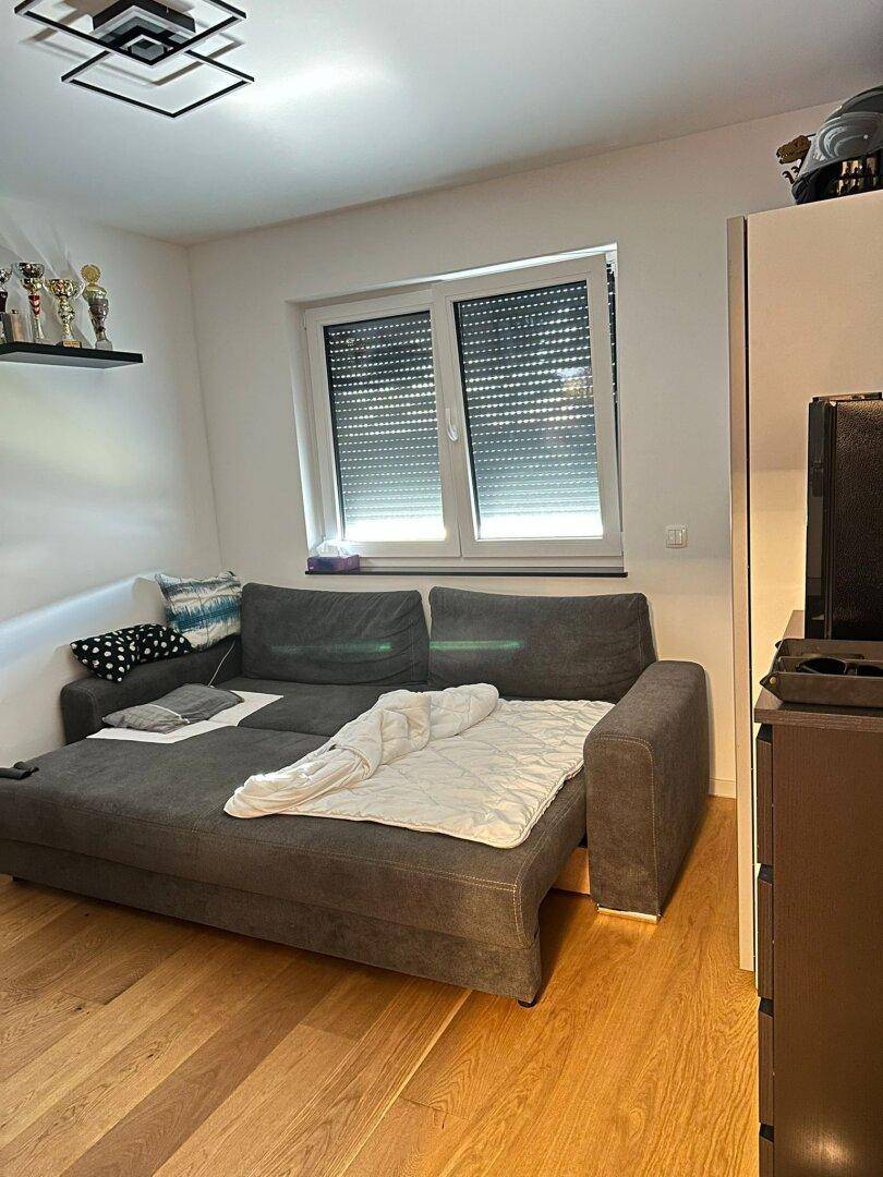 Gemütliches Wohnzimmer mit Schlafsofa, Holzboden und Fenster mit Rollladen.