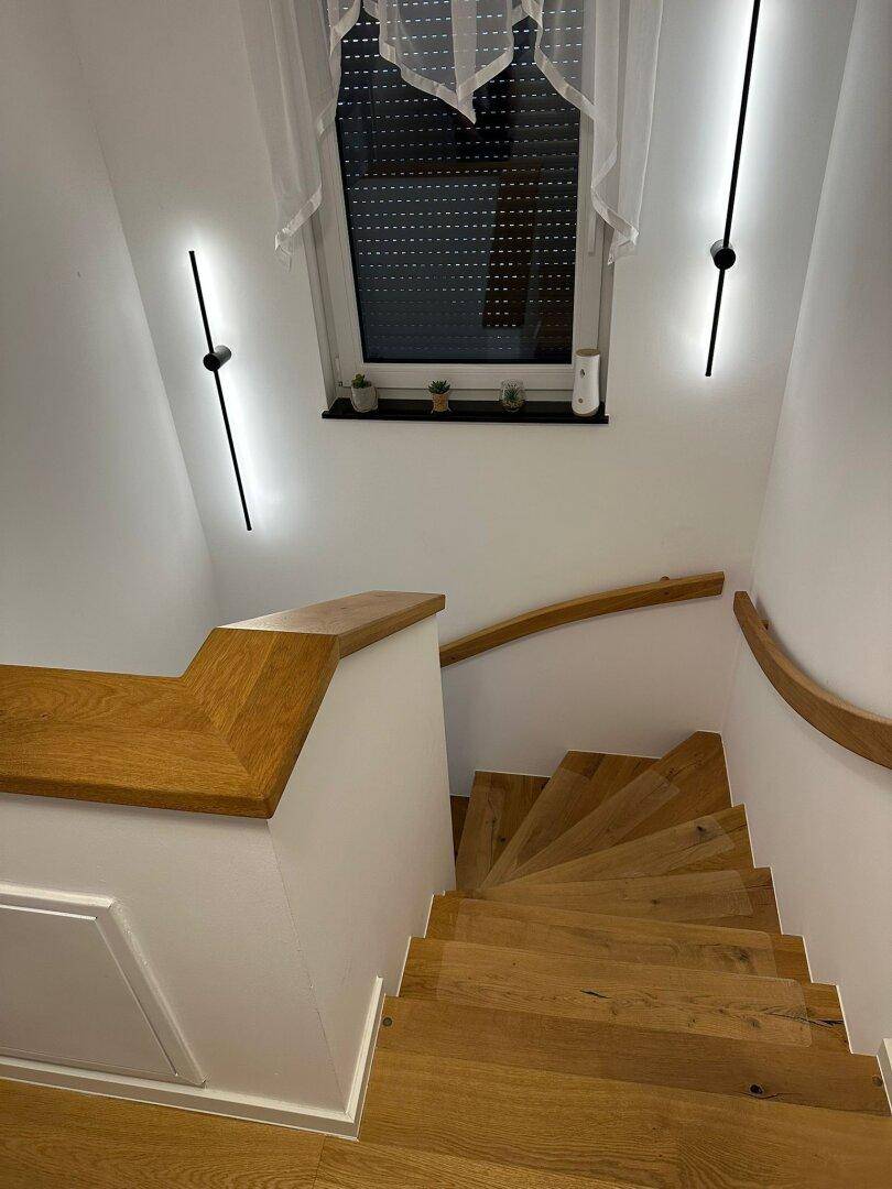 Helle Holztreppe mit Fenster, modernem Geländer und indirekter Beleuchtung.