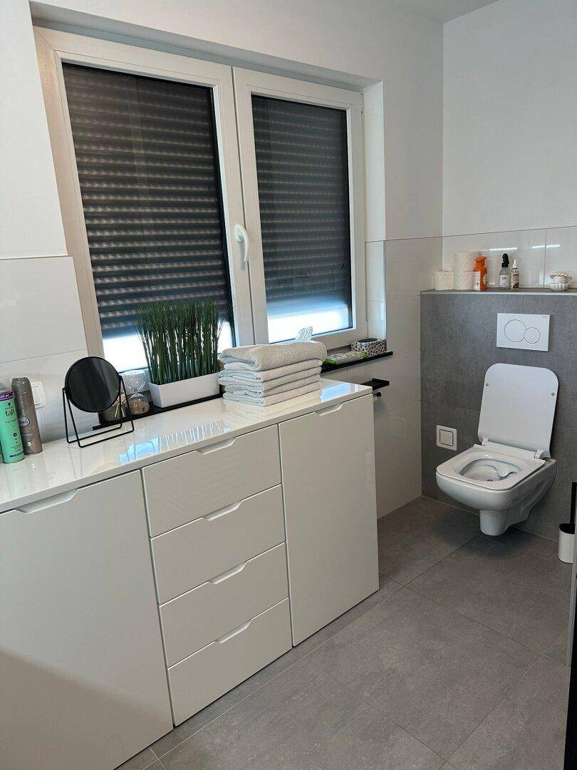 Modernes Badezimmer mit wandhängendem WC, breitem Waschtischunterschrank und Fenster.
