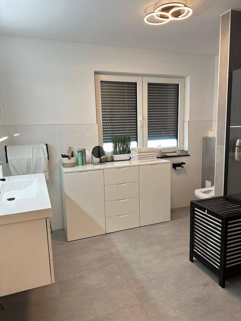 Geräumiges Badezimmer mit Doppelwaschtisch, wandhängendem WC und großem Fenster.
