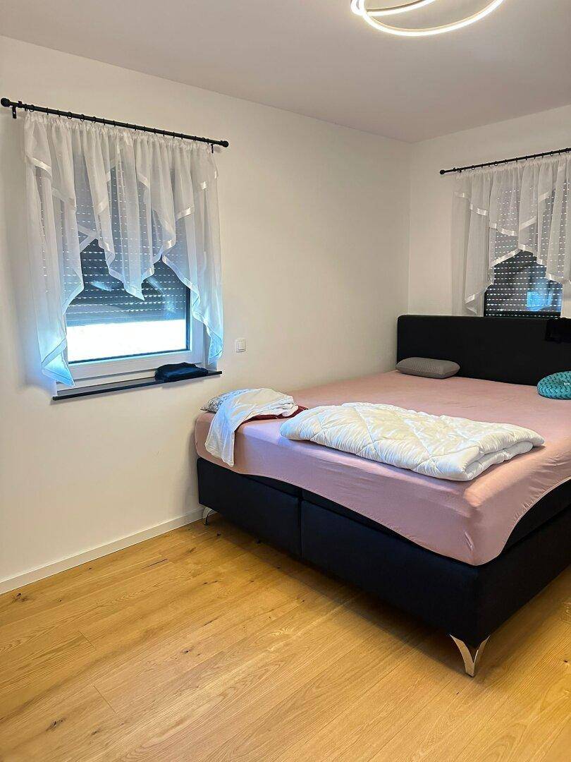 Helles Schlafzimmer mit Holzboden, Doppelbett und Fenster mit transparenten Vorhängen.