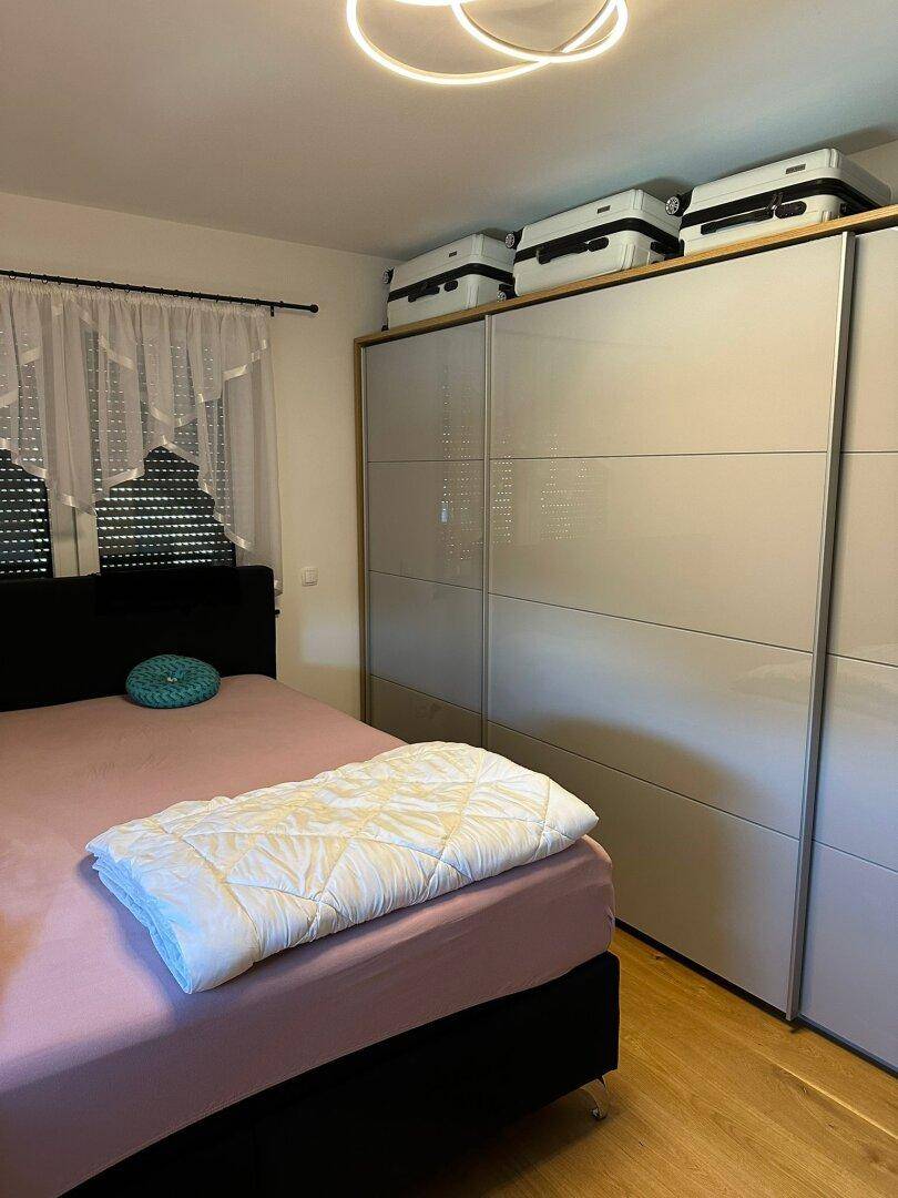 Schlafzimmer mit Doppelbett, großem Kleiderschrank und Fenster mit Vorhängen.