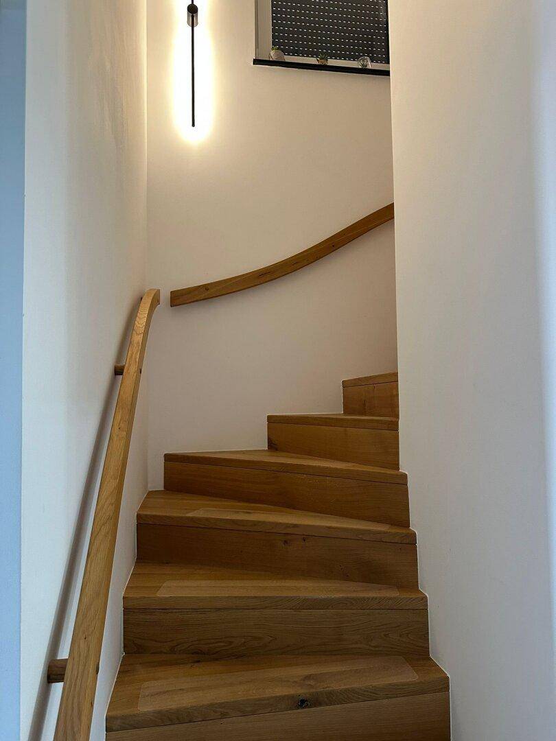 Moderne Holztreppe mit elegantem Handlauf und minimalistischer Beleuchtung.