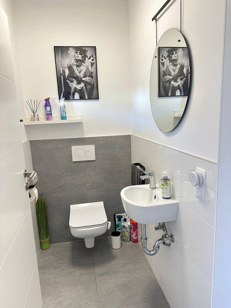 Kleines Gäste-WC mit wandhängendem WC, Handwaschbecken und modernem Spiegel.