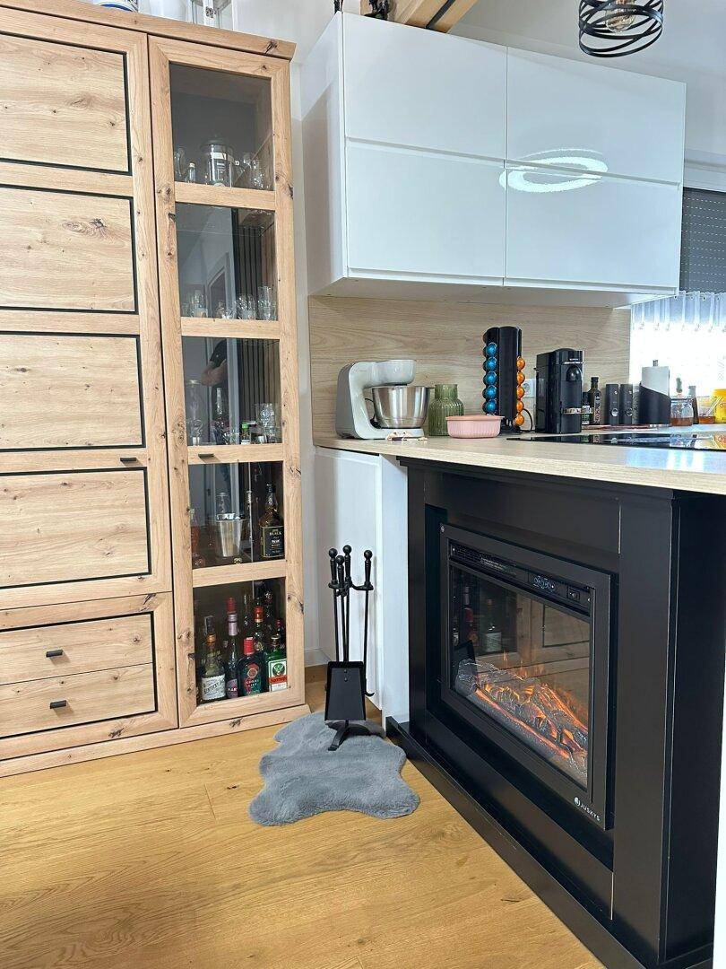 Moderne Küche mit Holzboden, weißen Oberschränken und integriertem Elektrokamin in der Kücheninsel.