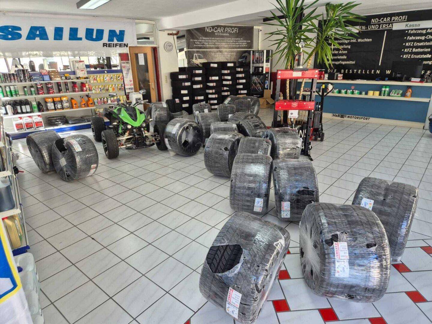 Ansicht des Geschäfts mit vielen verpackten Reifen, einem Quad-Bike und Regalen voller Autozubehör.