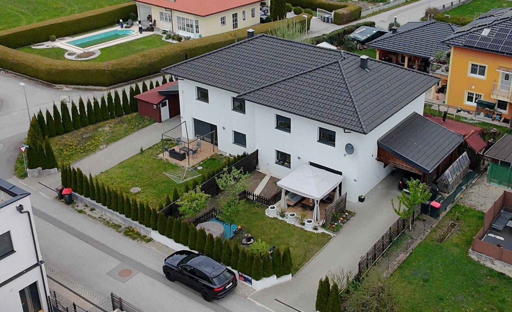 Übersicht des modernen Einfamilienhauses mit Garten, Carport und angrenzendem Nachbarschaftspool.