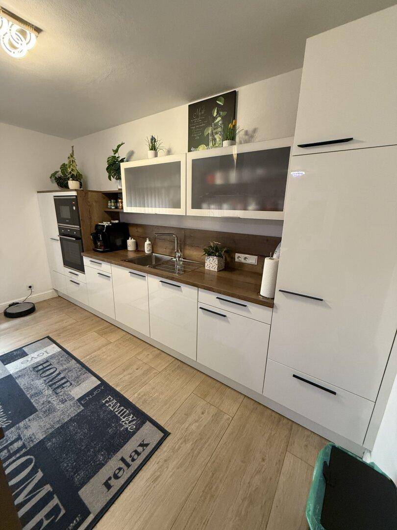 Helle Einbauküche mit weißen Hochglanzfronten, Holz-Arbeitsplatte und modernen Hängeschränken.