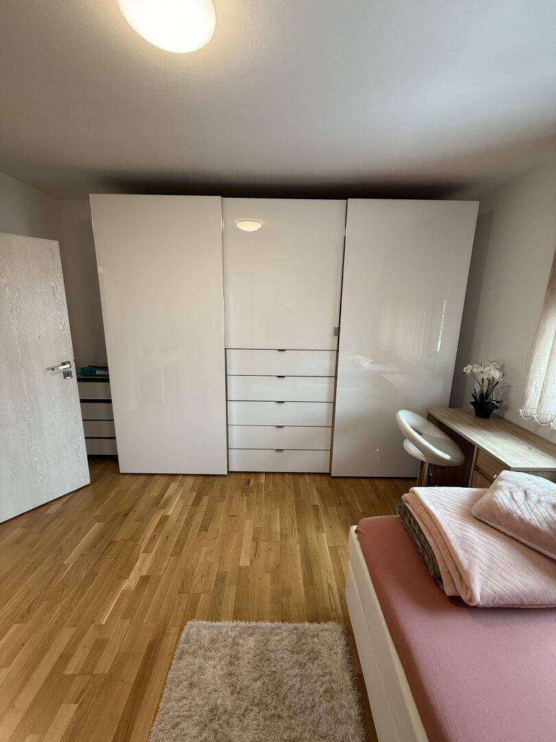 Geräumiger weißer Kleiderschrank mit Hochglanzfronten und integrierten Schubladen im Schlafzimmer.