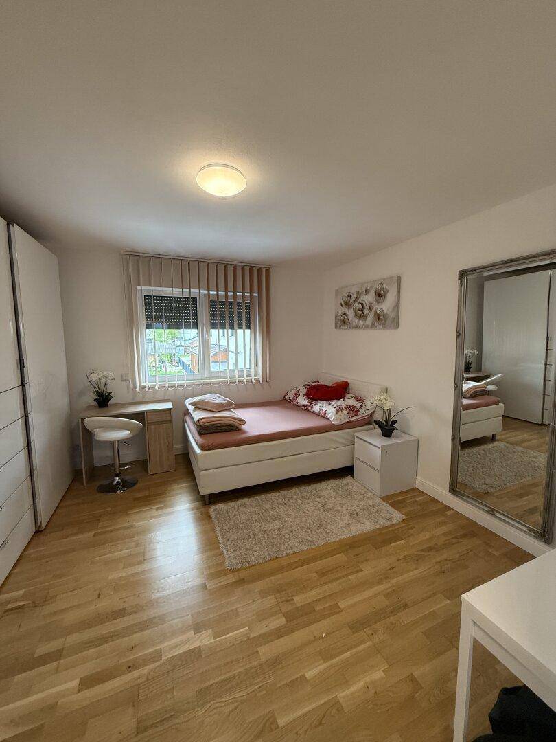 Gemütliches Schlafzimmer mit hellem Parkettboden, großem Fenster und modernem Kleiderschrank.