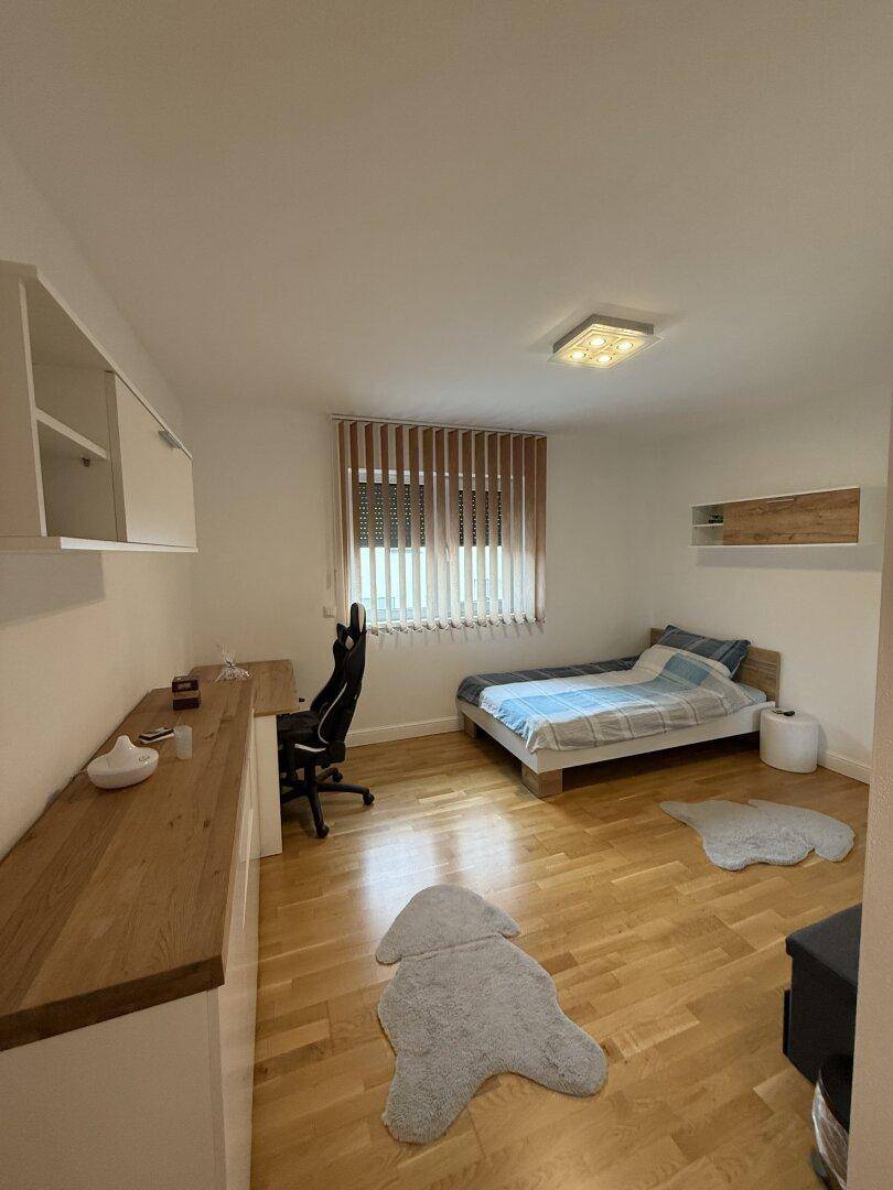 Helles Schlafzimmer mit Holzparkett, Schreibtisch und Einzelbett, ideal als Kinder- oder Gästezimmer.