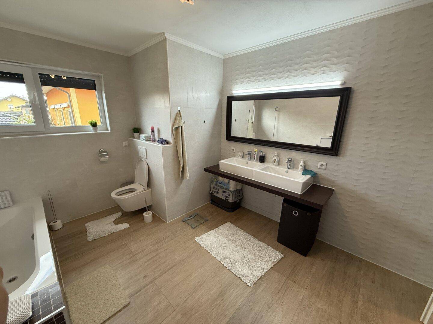 Modernes Badezimmer mit Doppelwaschbecken, Wand-WC und Fenster für natürliche Belüftung.