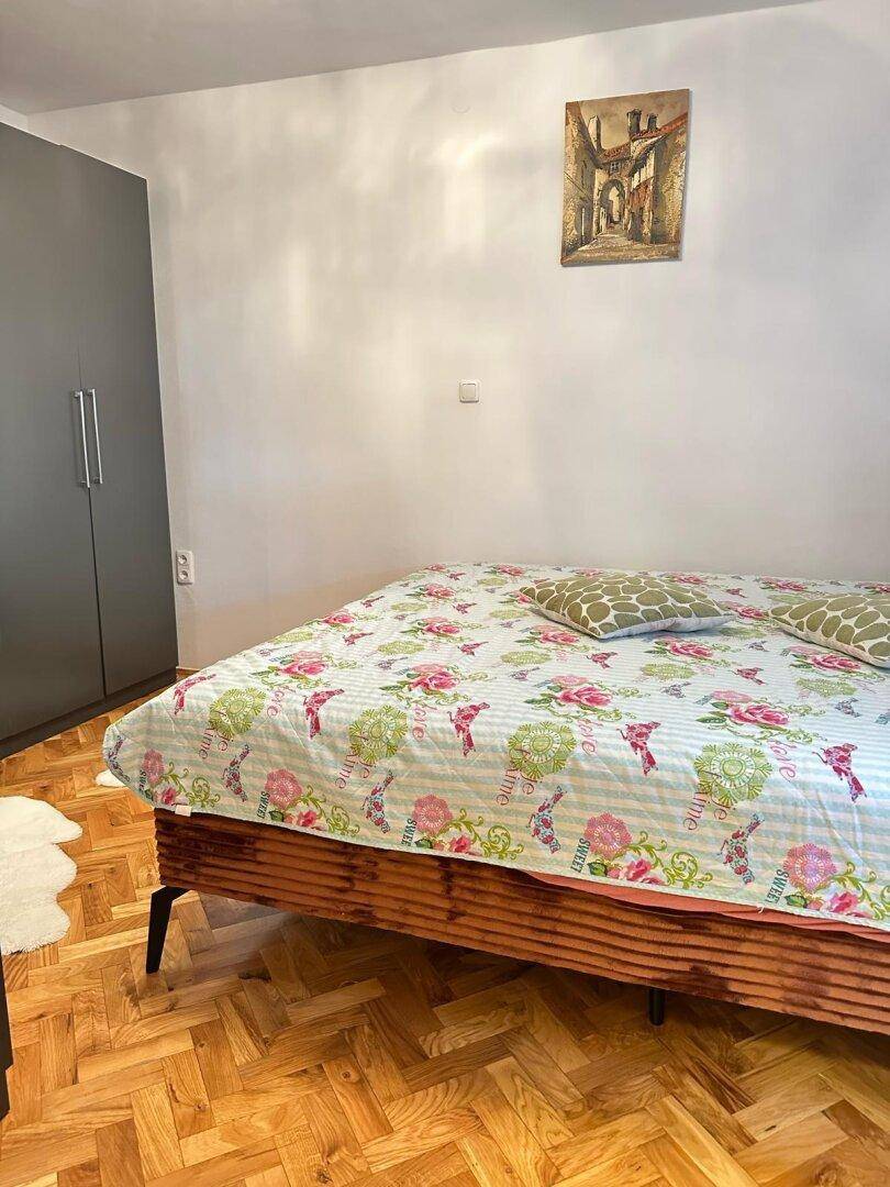 Schlafzimmer mit Holzboden, floral gemustertem Bett und grauem Kleiderschrank.