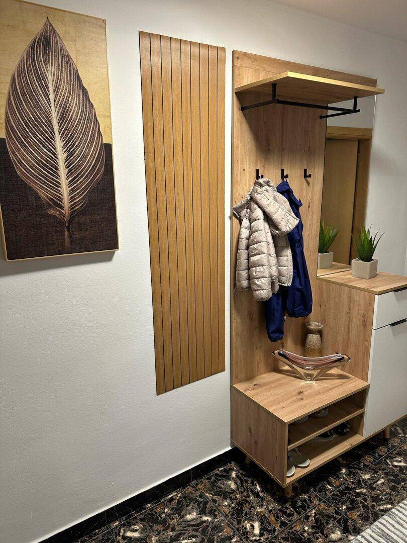 Moderner Eingangsbereich mit Garderobe aus Holz, Spiegel und dekorativem Wandbild.