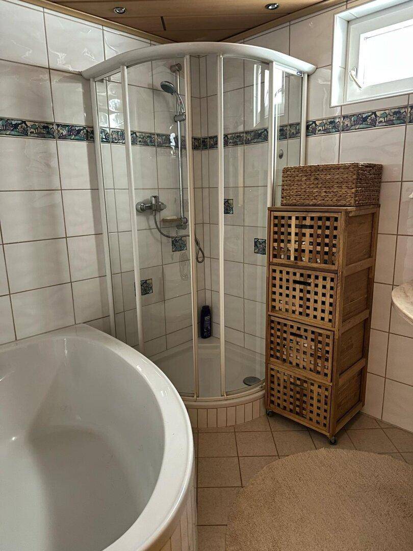 Badezimmer mit Eckbadewanne, Duschkabine und Holzschrank unter einer Dachschräge.