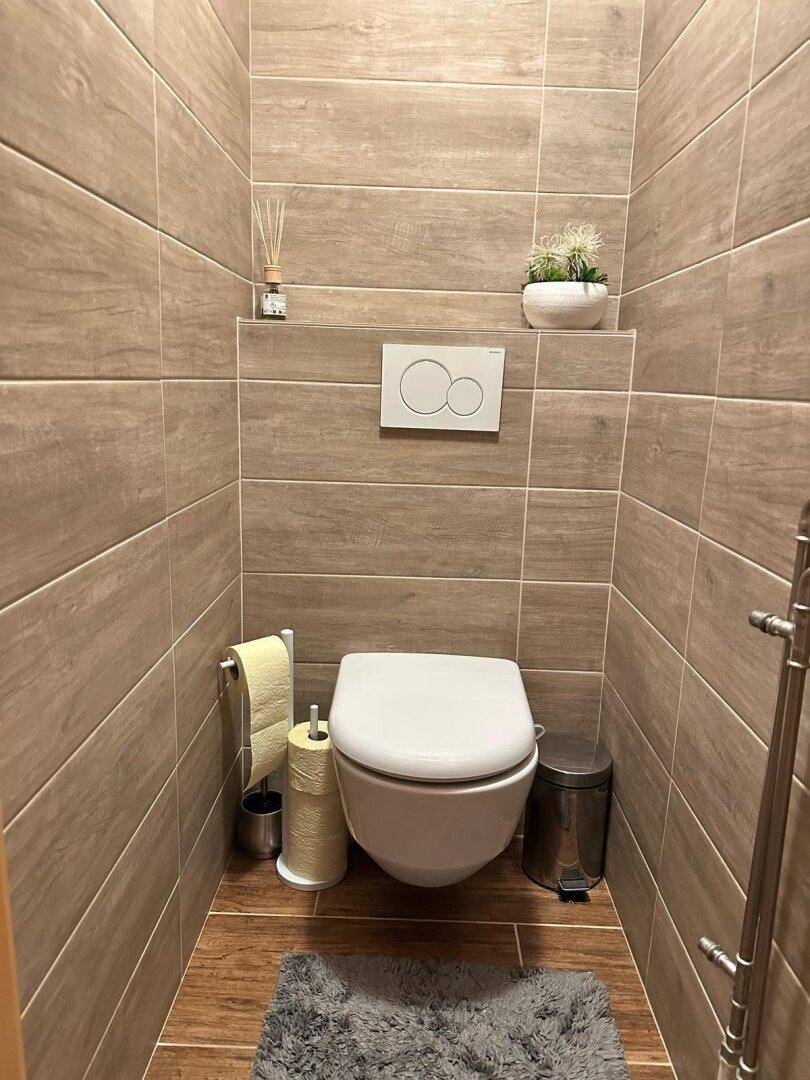 Modernes Gäste-WC mit Wand-WC, beigen Fliesen und kleinem Dekorationselement.
