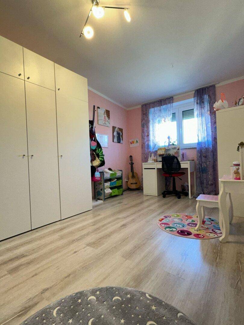 Kinderzimmer mit rosa Wänden, Schreibtisch, Kleiderschrank und hellem Laminatboden.