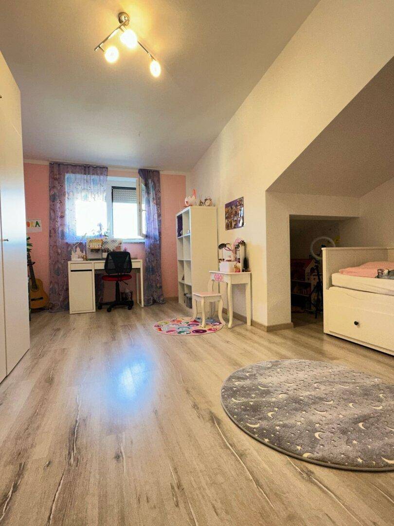 Geräumiges Kinderzimmer mit Schreibtisch, Regal und einem Bett in einer Nische.