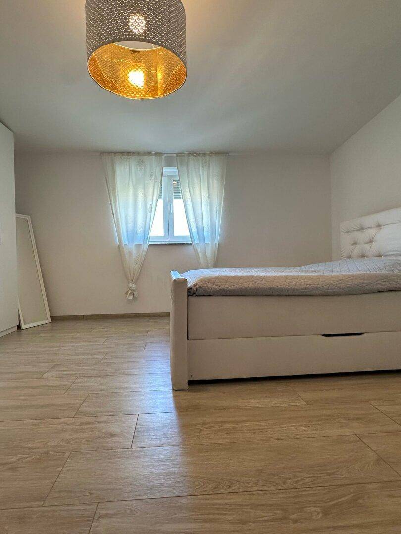 Helles Schlafzimmer mit weißem Bett, Vorhängen und modernem Holzboden.