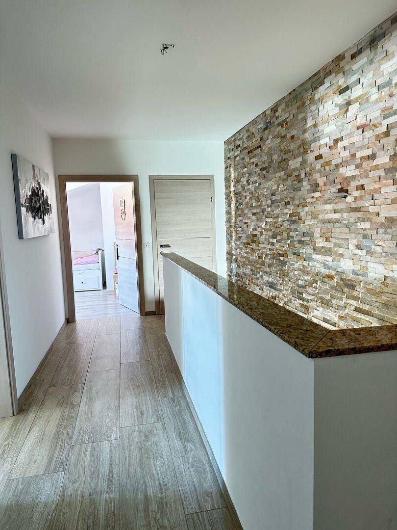 Heller Flur im Obergeschoss mit Steinwand, Granitgeländer und Holzboden.
