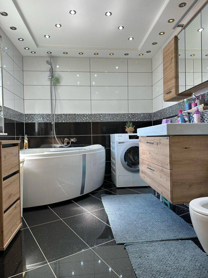 Modernes Badezimmer mit Badewanne, Waschmaschine, Waschbecken und Einbaustrahlern.