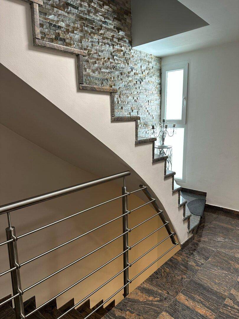 Treppenhaus mit moderner Steinwandverkleidung, Edelstahlgeländer und Fenster.
