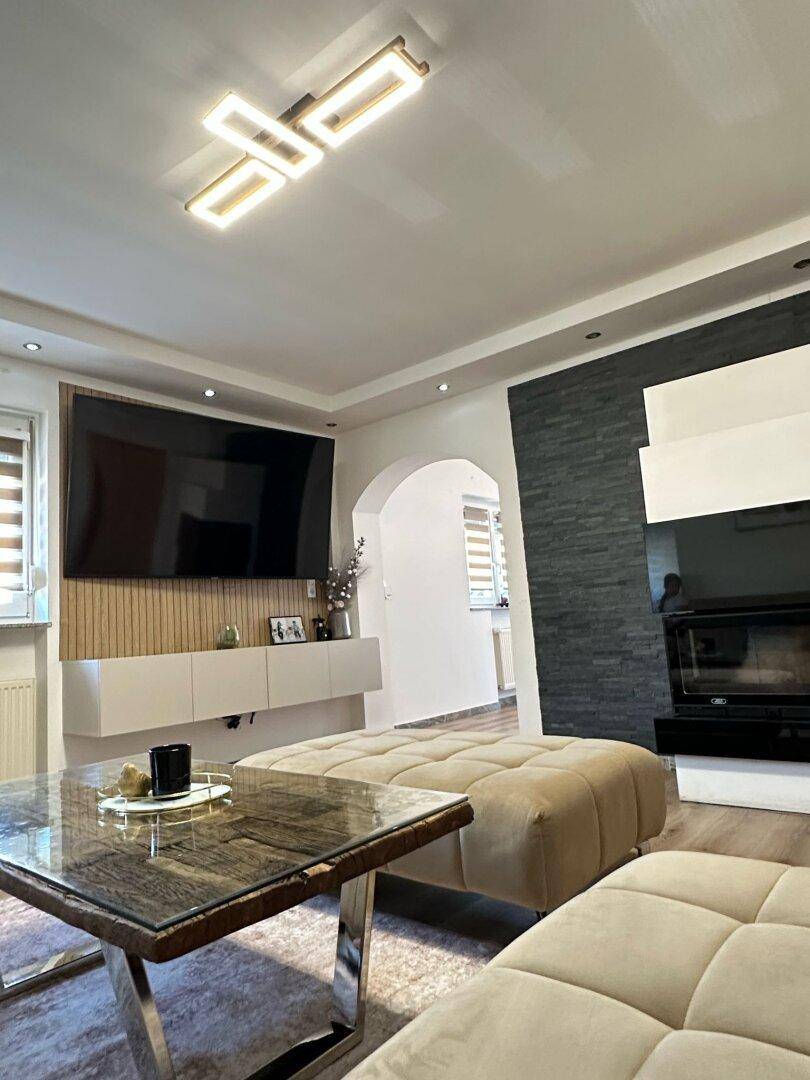 Helles Wohnzimmer mit modernem Kamin, großem Fernseher und Couchtisch mit Glasplatte.