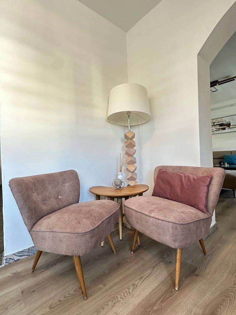 Gemütliche Sitzecke mit zwei rosa Sesseln, Beistelltisch und Stehlampe in einem hellen Raum.