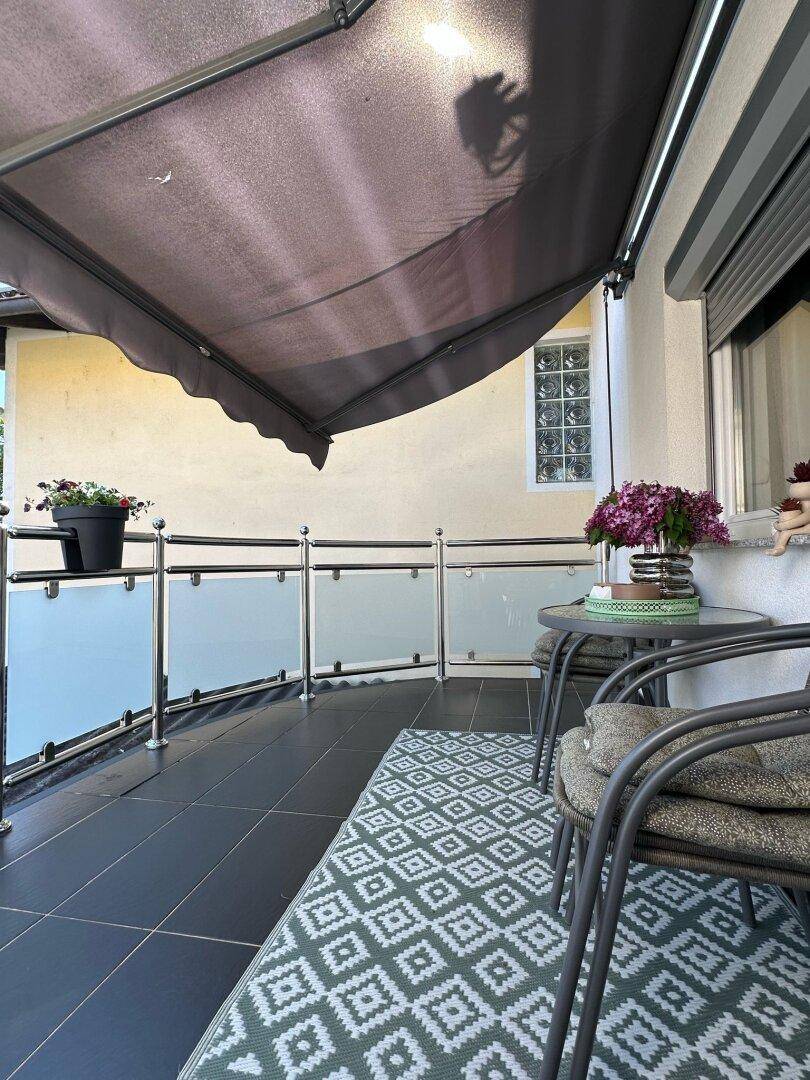 Gemütlicher Balkon mit dunklen Fliesen, Teppich und ausziehbarer Markise für angenehme Stunden im Freien.