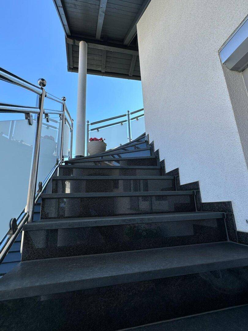 Elegante Außentreppe mit dunklen Granitstufen und modernen Glasgeländern.