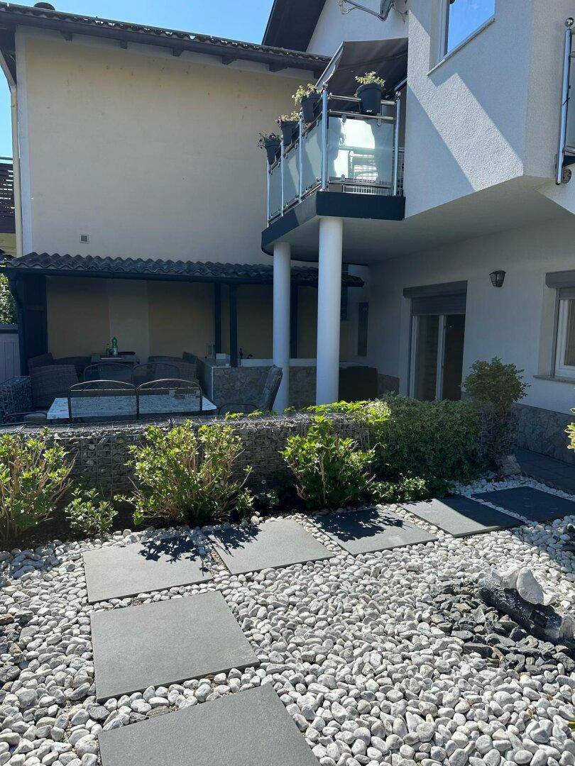 Außenbereich des Hauses mit Kiesgarten, Trittsteinen und überdachtem Sitzbereich im Freien.