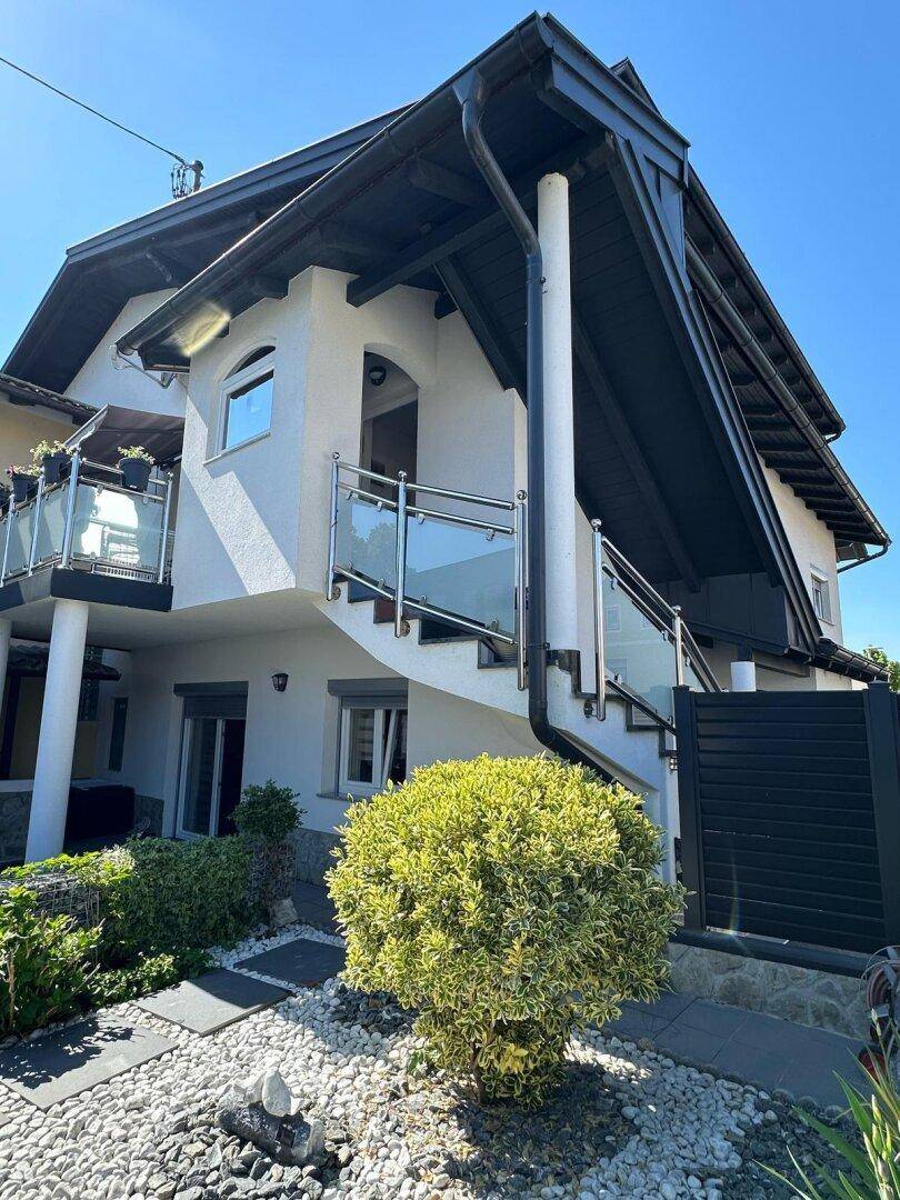 Seitenansicht des Hauses mit Balkon, Außentreppe und gepflegter Gartenanlage.