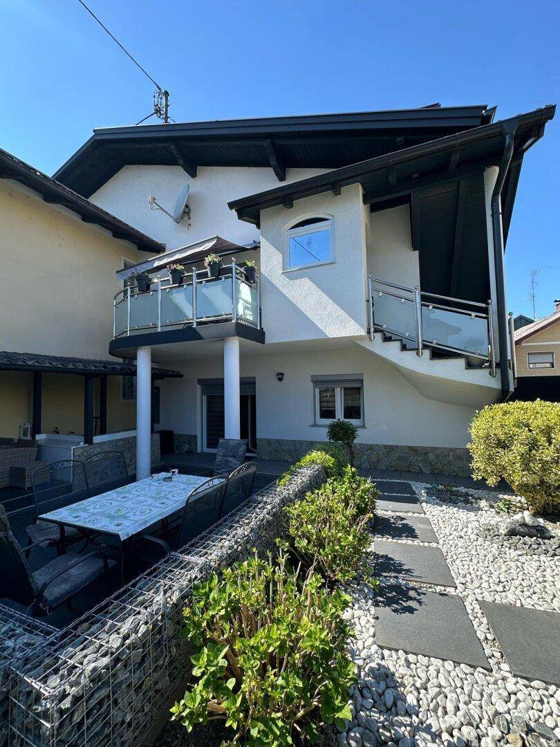 Weitläufiger Außenbereich mit Kiesgarten, überdachtem Essbereich und Zugang zum Balkon über eine Außentreppe.