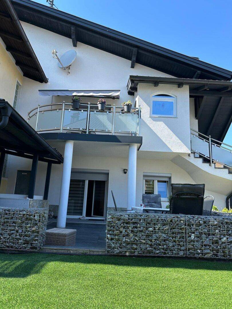 Außenbereich des Hauses mit Rasenfläche, Terrasse und Balkon mit Glasgeländer.