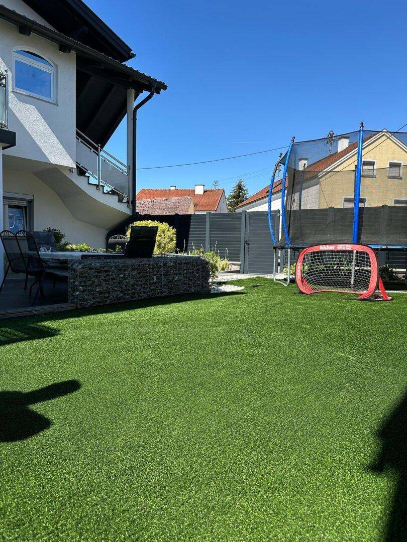 Gartenbereich mit Kunstrasen, Trampolin und Fußballtor, ideal für Kinder und Freizeitaktivitäten.
