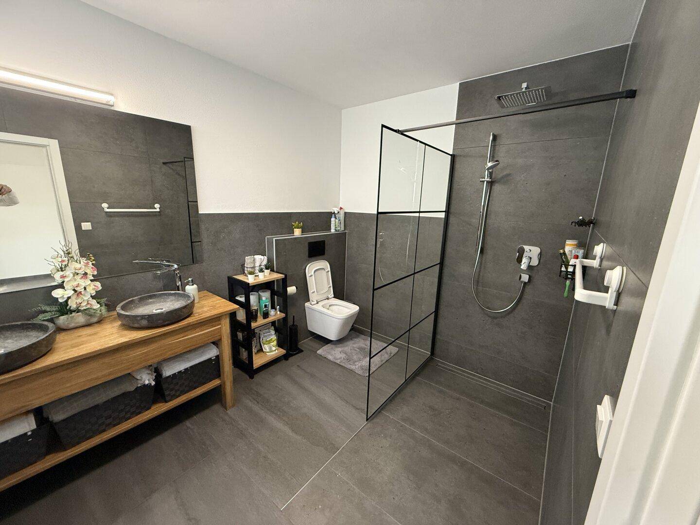 Modernes Badezimmer mit dunklen Fliesen, Doppelwaschbecken und großer begehbarer Dusche.