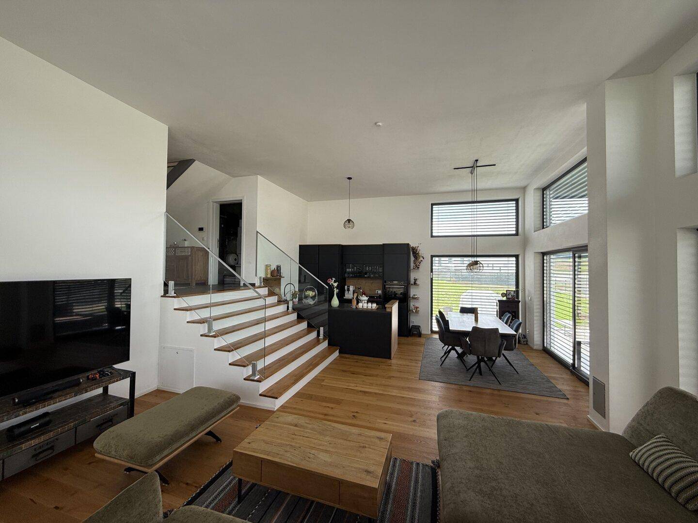 Heller offener Wohn-Essbereich mit Holzboden, moderner Küche und Treppe mit Glasgeländer.