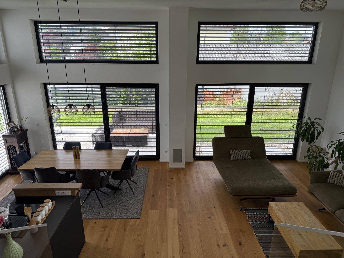 Weitläufiger Wohn-Essbereich mit Holzboden, Esstisch und Lounge-Bereich, hell durch große Fenster.