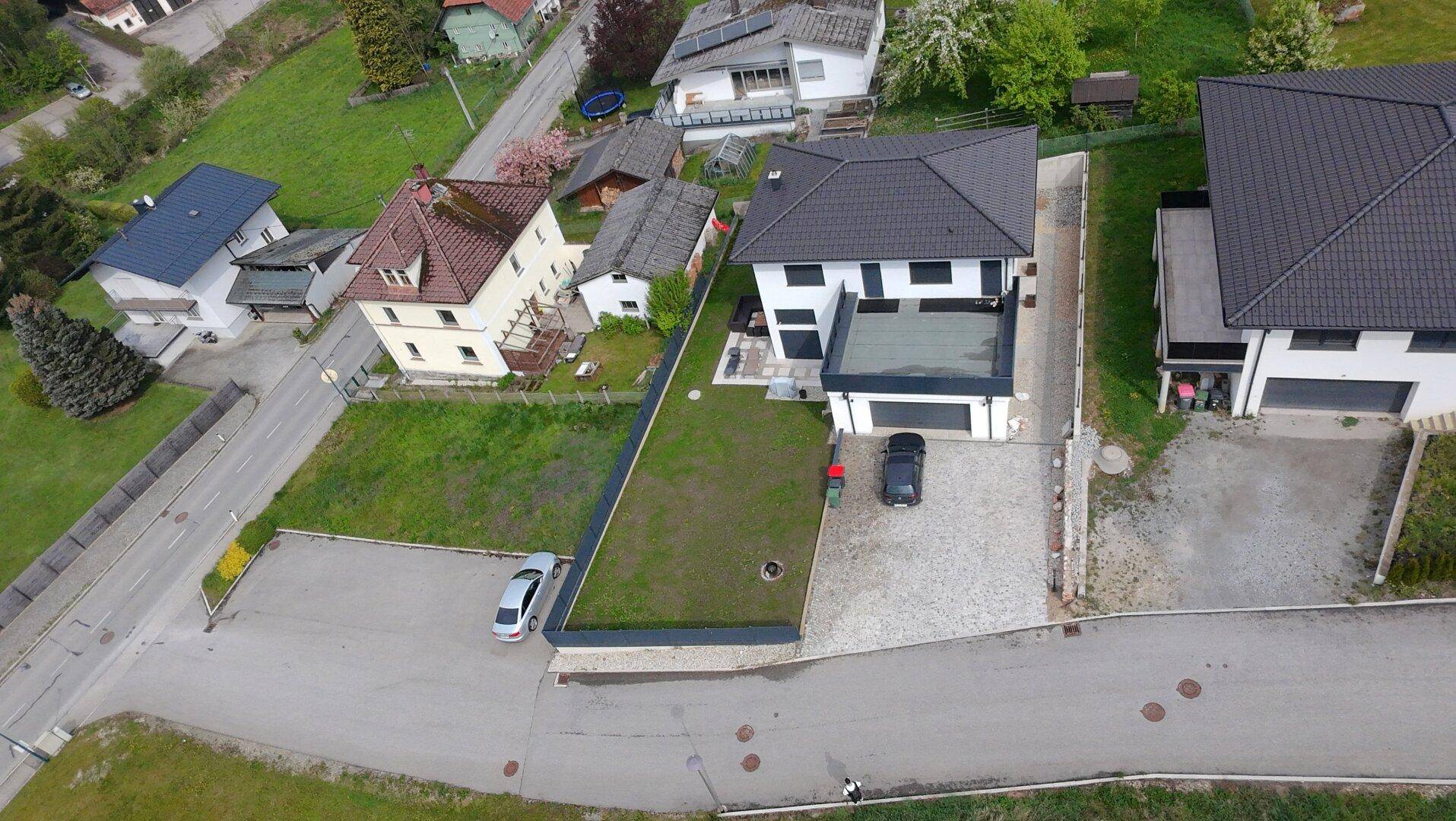 Luftaufnahme eines modernen Einfamilienhauses mit Garten, Garage und Zufahrt in Wohngegend.