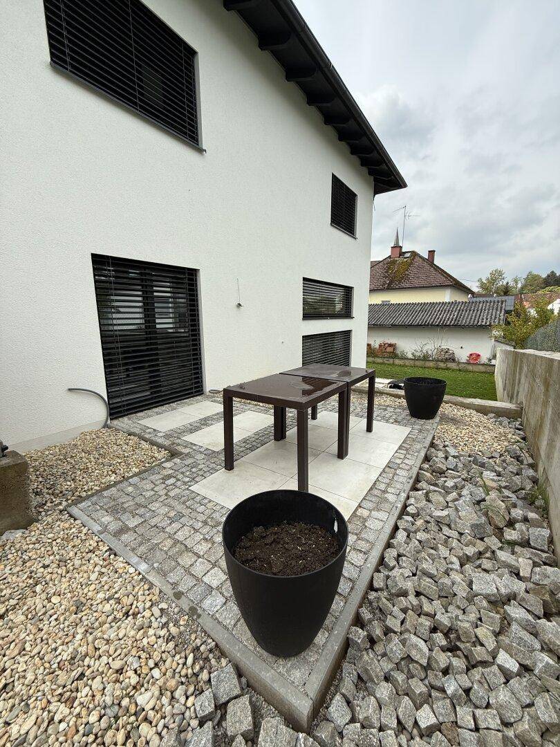 Kleine gepflasterte Terrasse mit Steinelementen und einem Gartentisch neben dem Haus.