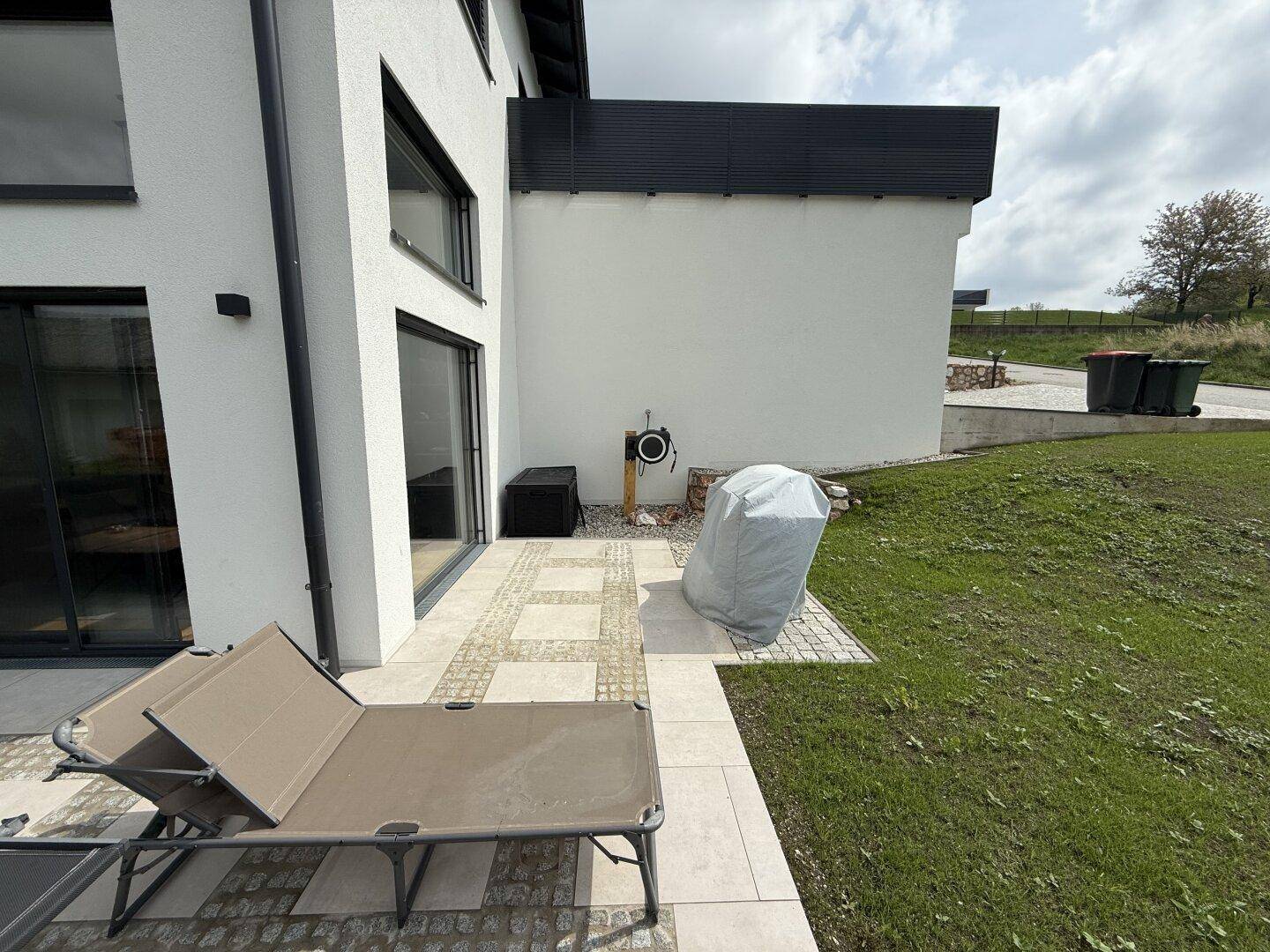Gepflasterte Terrasse am Haus mit Sonnenliegen und Zugang zum Gartenbereich.