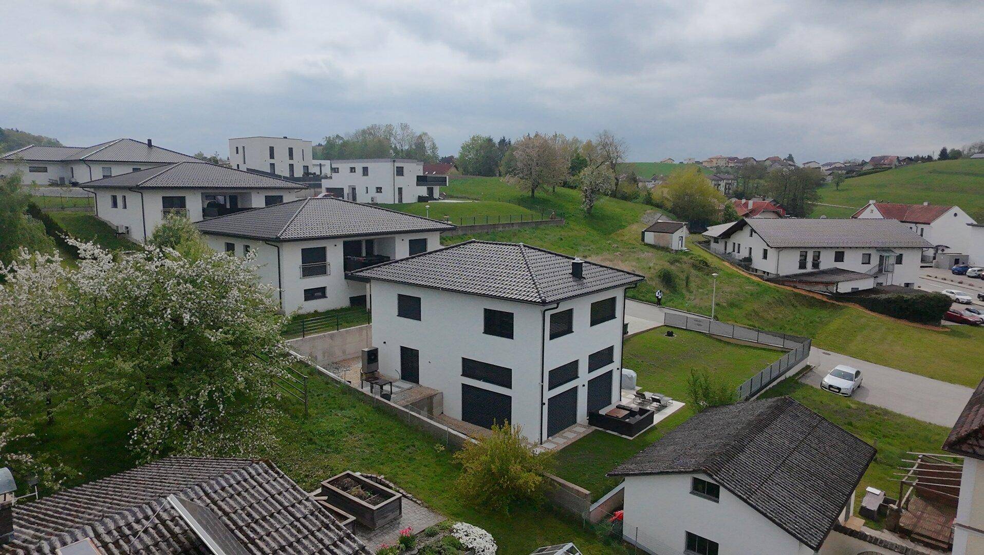 Mehrere moderne Einfamilienhäuser in einer Neubausiedlung mit grüner Hügellandschaft im Hintergrund.
