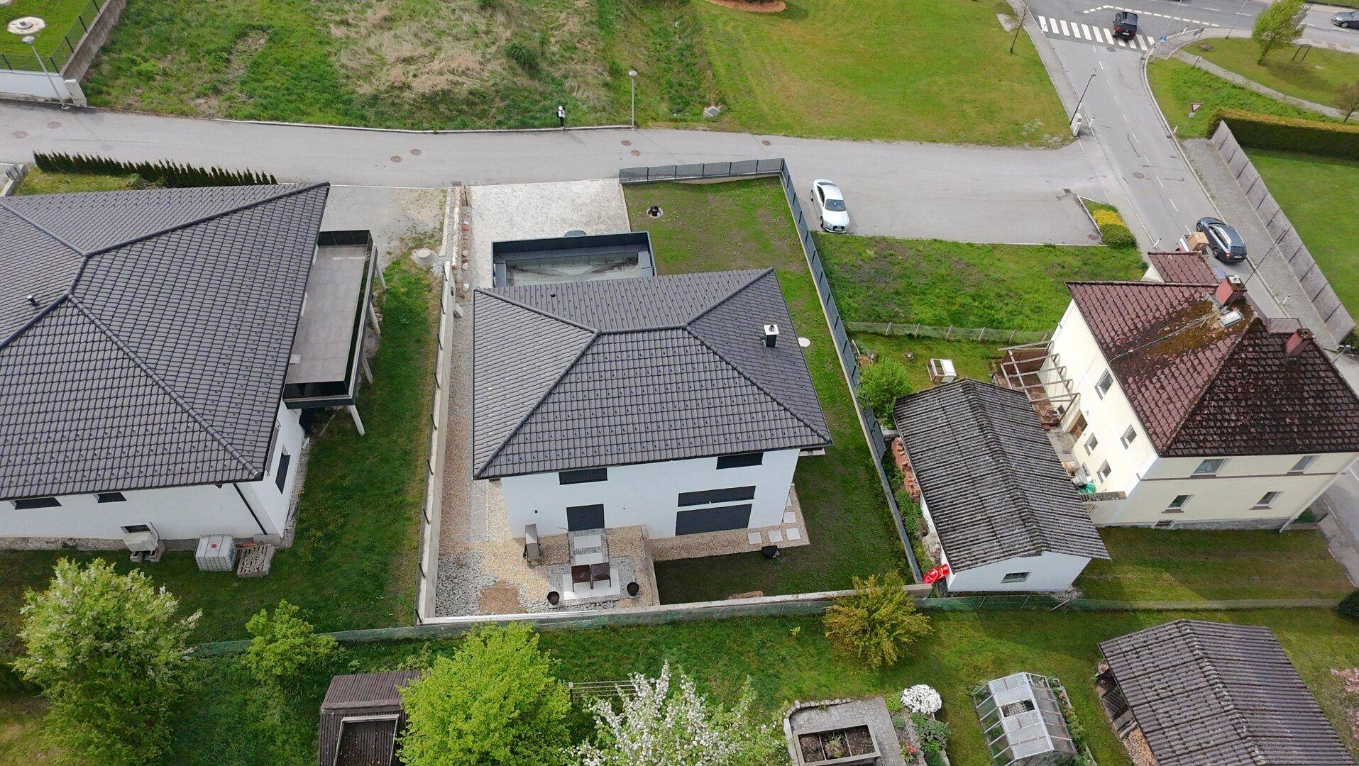 Vogelperspektive eines Neubaus mit Satteldach, Garten und umliegenden Häusern in ländlicher Umgebung.