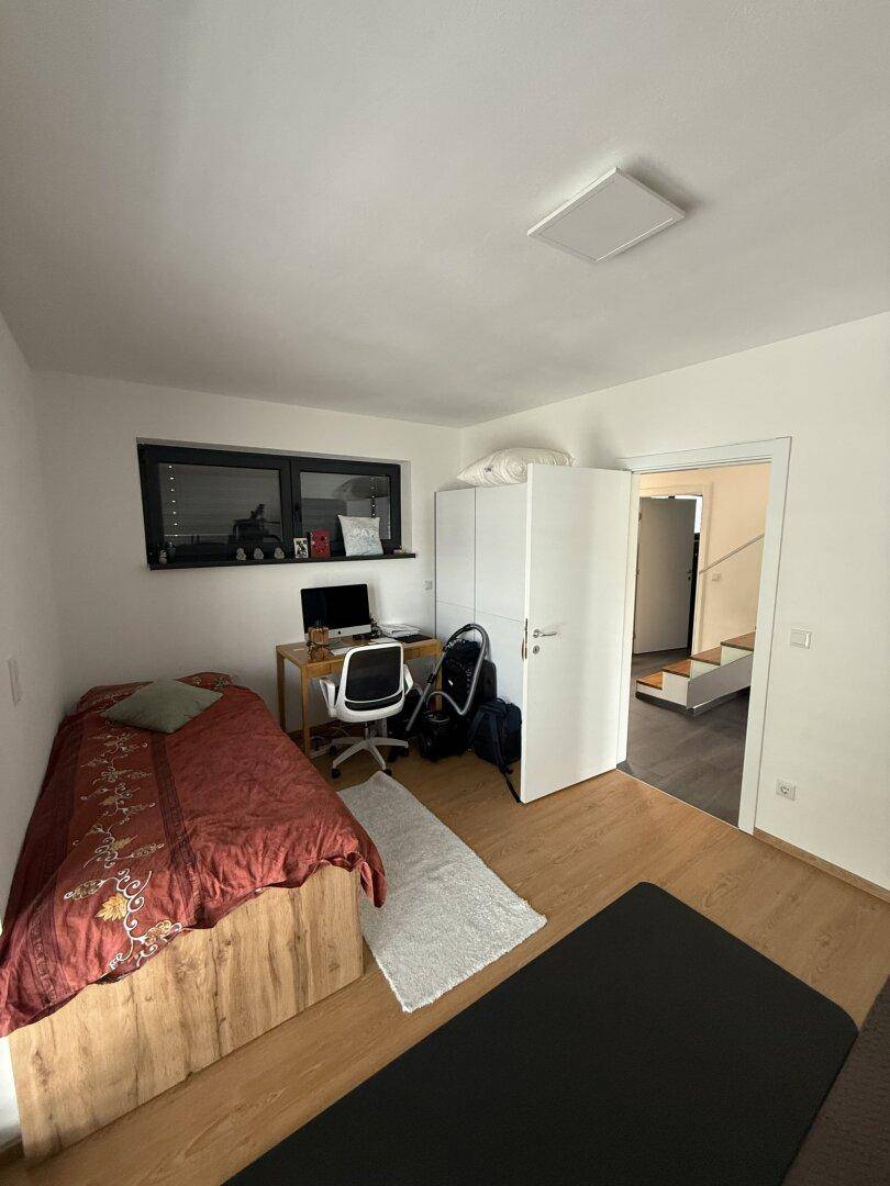 Schlafzimmer mit Holzboden, Einzelbett, Schreibtisch und weißem Kleiderschrank.