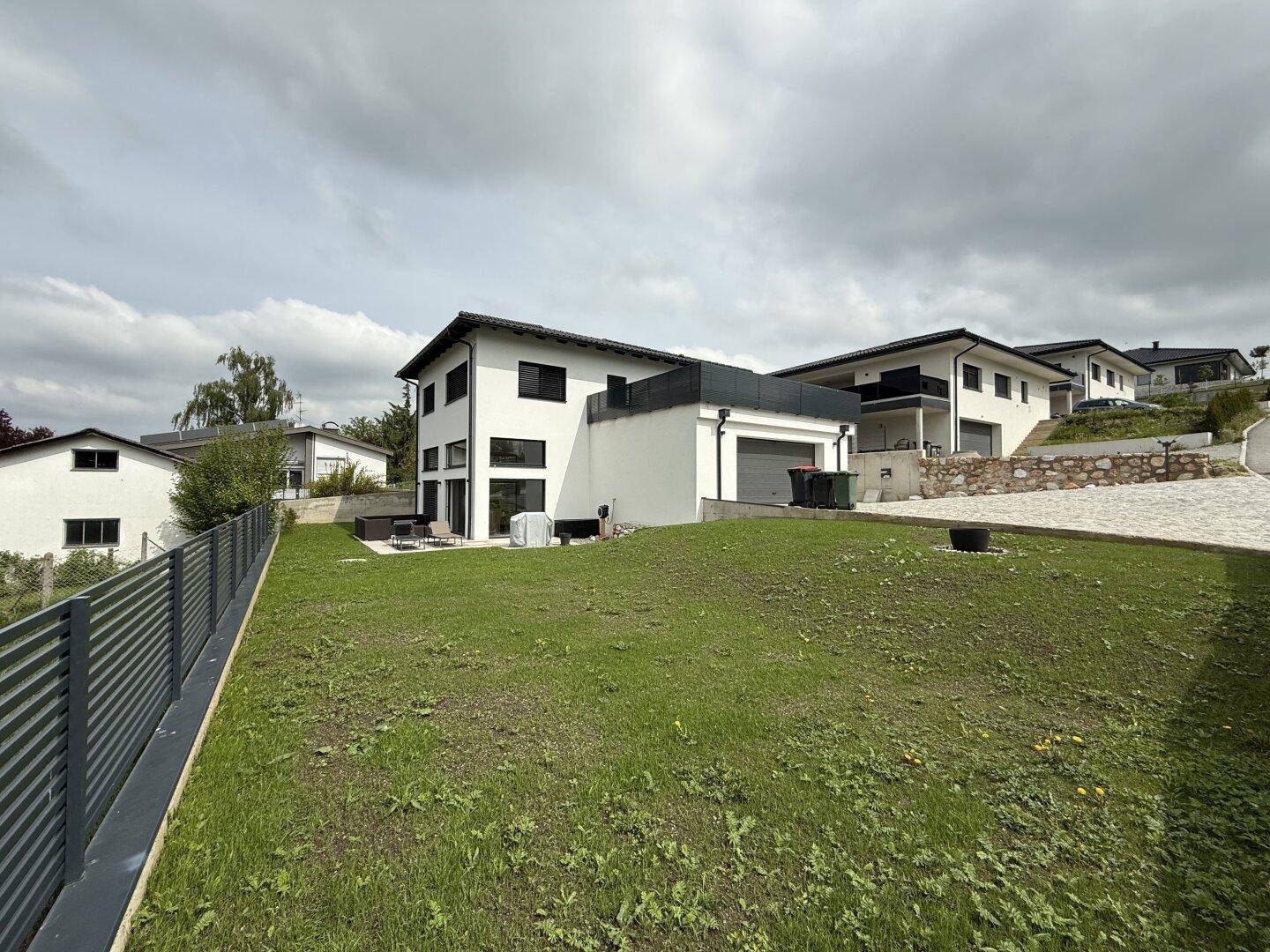 Modernes Einfamilienhaus mit weißer Fassade, großen Fenstern und weitläufigem Gartenbereich.